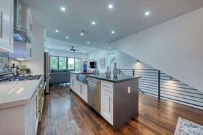 Een moderne keuken met een centraal eiland, houten vloeren en een trap naar een verdieping erboven.