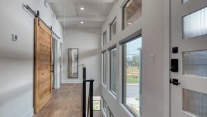 A modern hallway with a wooden sliding door, large windows, and a view of the outside. - Urban Modern Luxury Group Rental in Lavaca (San Antonio)