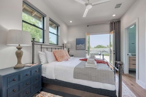 A bedroom with a large bed, a nightstand, a lamp, and a view of the outdoors.