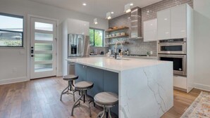 A modern kitchen with a marble island, stainless steel appliances, and a large window. - Urban Modern Luxury Group Rental in Lavaca (San Antonio)