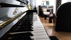 Un piano dans une pièce dont le sol est en bois, avec une chaise et une petite table.