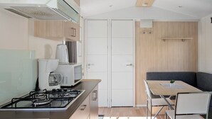 Cocina compacta con estufa a gas, microondas y cafetera. Hay una zona de comedor con mesa y sillas.