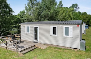 A small, single-story mobile home with a deck and a small outdoor table and chairs.