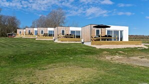 Una hilera de cabañas modernas de madera con ventanas amplias y un campo de césped al fondo.