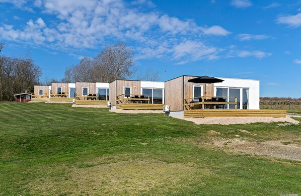 A row of modern, wooden cabins with large windows and a grassy field in the background.