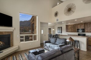 A spacious living area with a fireplace, a large gray sofa, and a kitchen with wooden cabinets and a microwave.