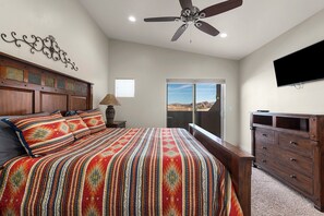 Relax in this serene bedroom with a large bed, ceiling fan, and flat-screen TV, plus a dresser and window with a mountain view.