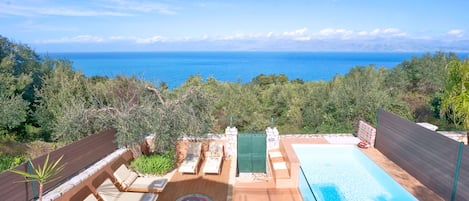 A pool area with lounge chairs and a view of the sea.