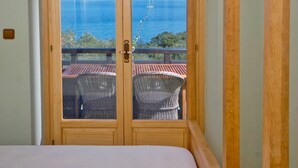Een slaapkamer met een groot raam met uitzicht op zee, houten balken en een bed met een witte dekbedovertrek.
