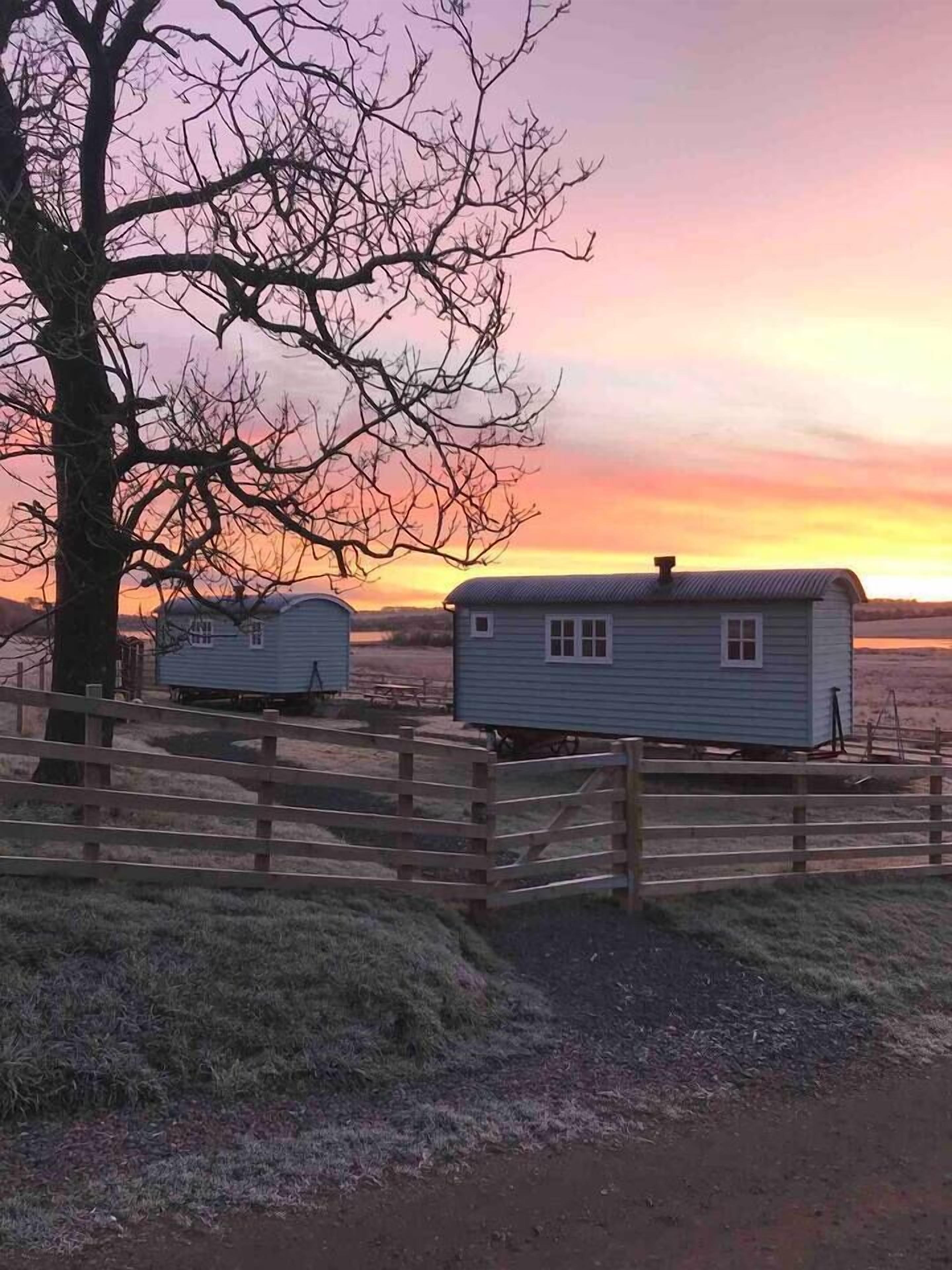 Un entorno rural con una valla de madera y dos casas móviles.