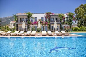 Un hotel con piscina, sillas de descanso y sombrillas.