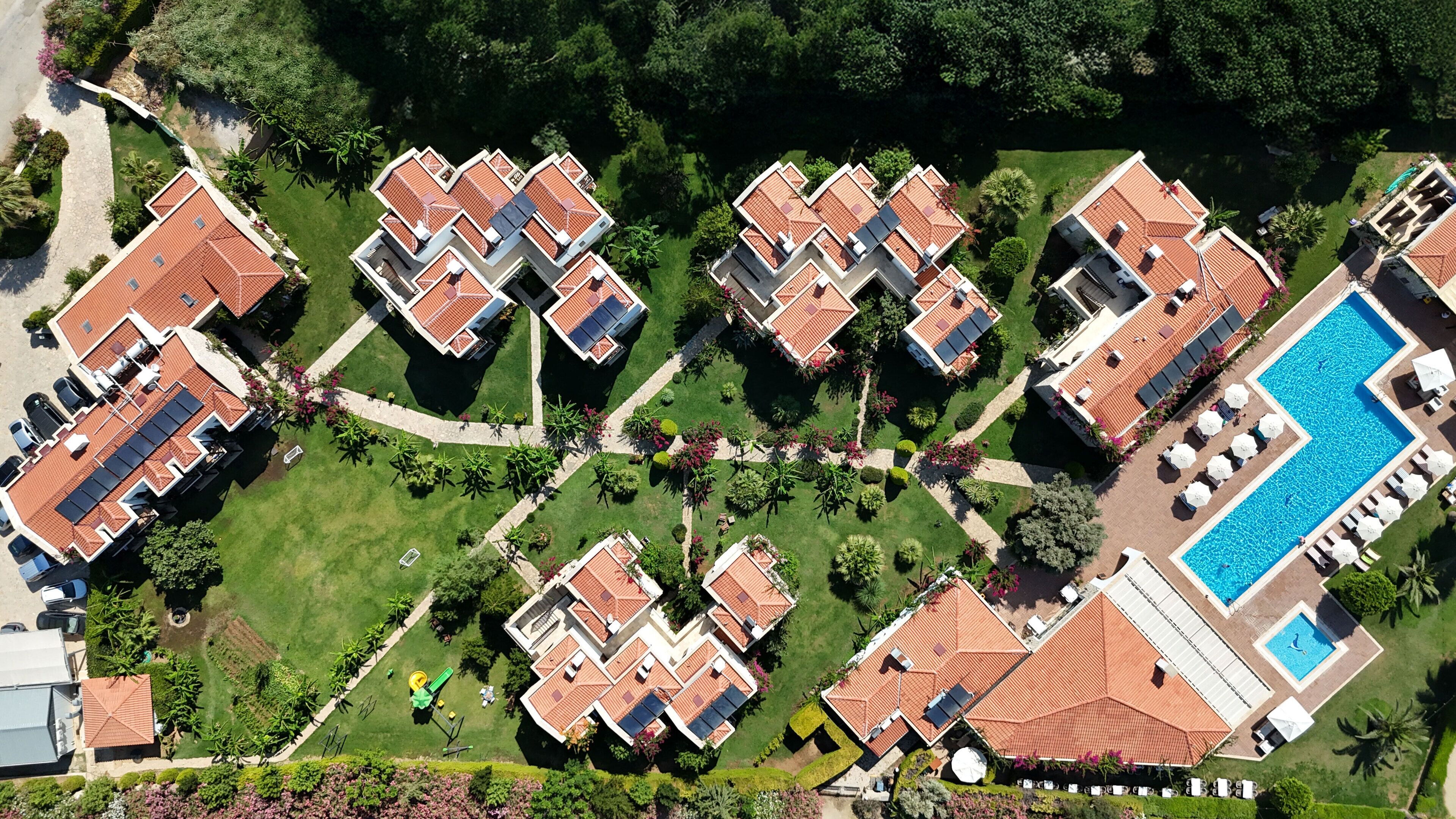 An aerial view of a residential complex with multiple apartment buildings, a swimming pool, and well-maintained gardens.