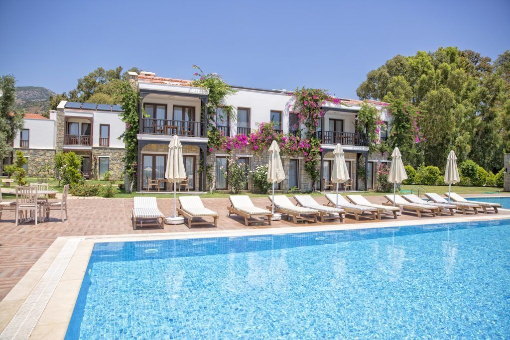 A poolside area with lounge chairs and umbrellas, a clear blue pool, and a building with balconies and greenery.