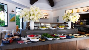 Buffet com diversos alimentos e flores brancas em vasos.
