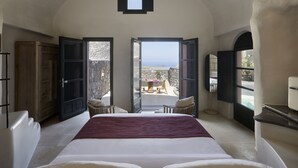 Een slaapkamer met een groot bed, uitzicht op zee door open deuren en een stenen muur.