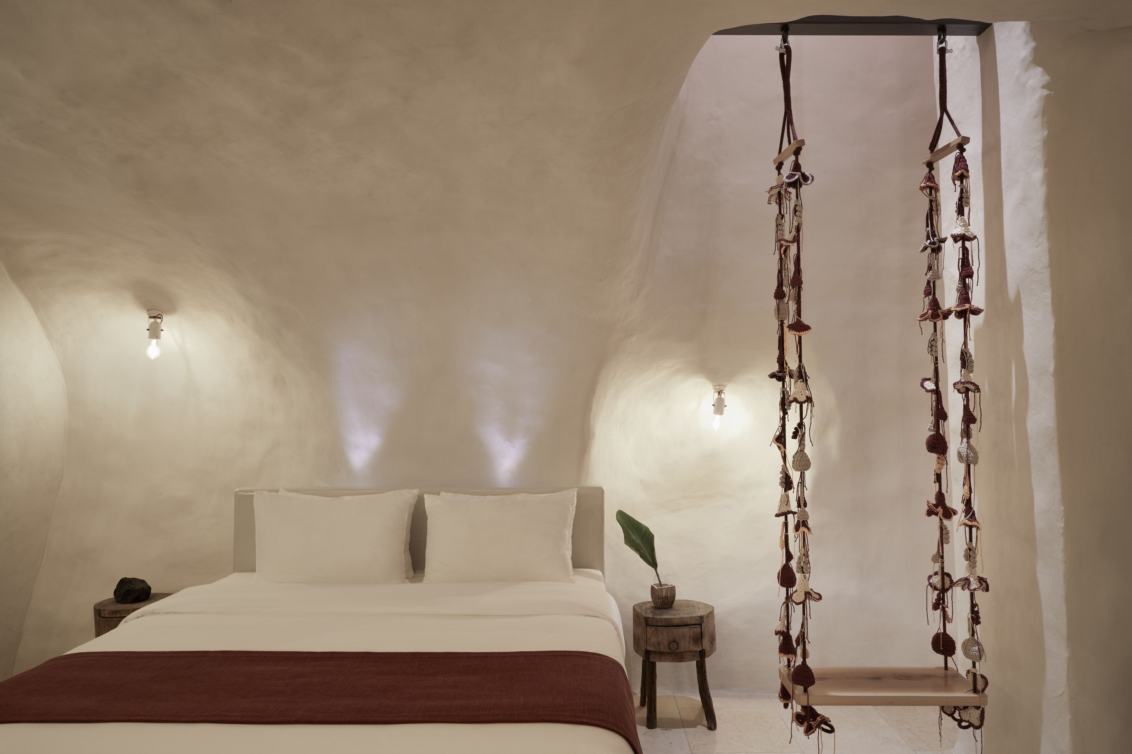 Een slaapkamer met een bed, nachtkastje, hangende decoraties en een wandlamp.