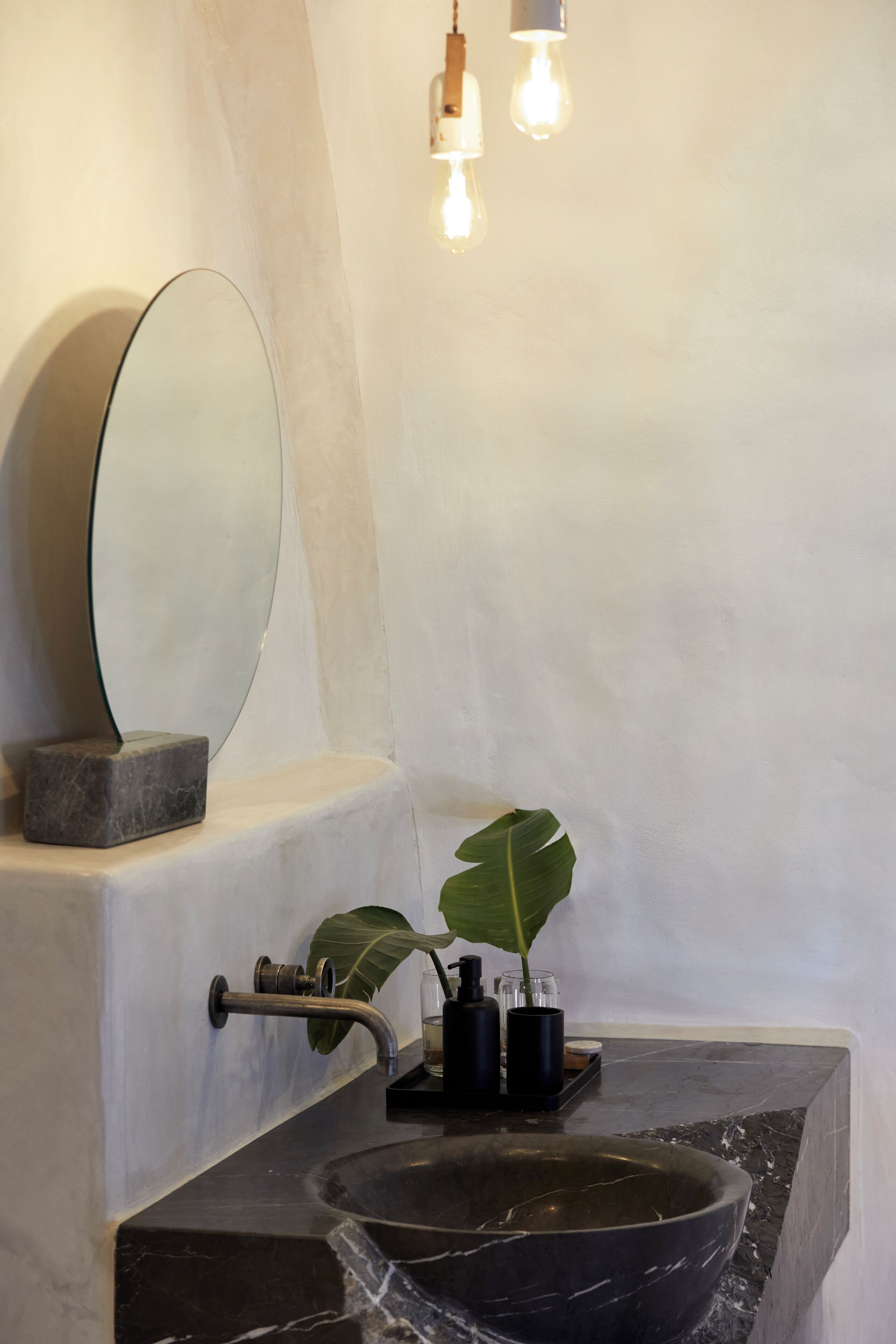 A bathroom with a marble sink, a large mirror, a potted plant, and a light fixture.