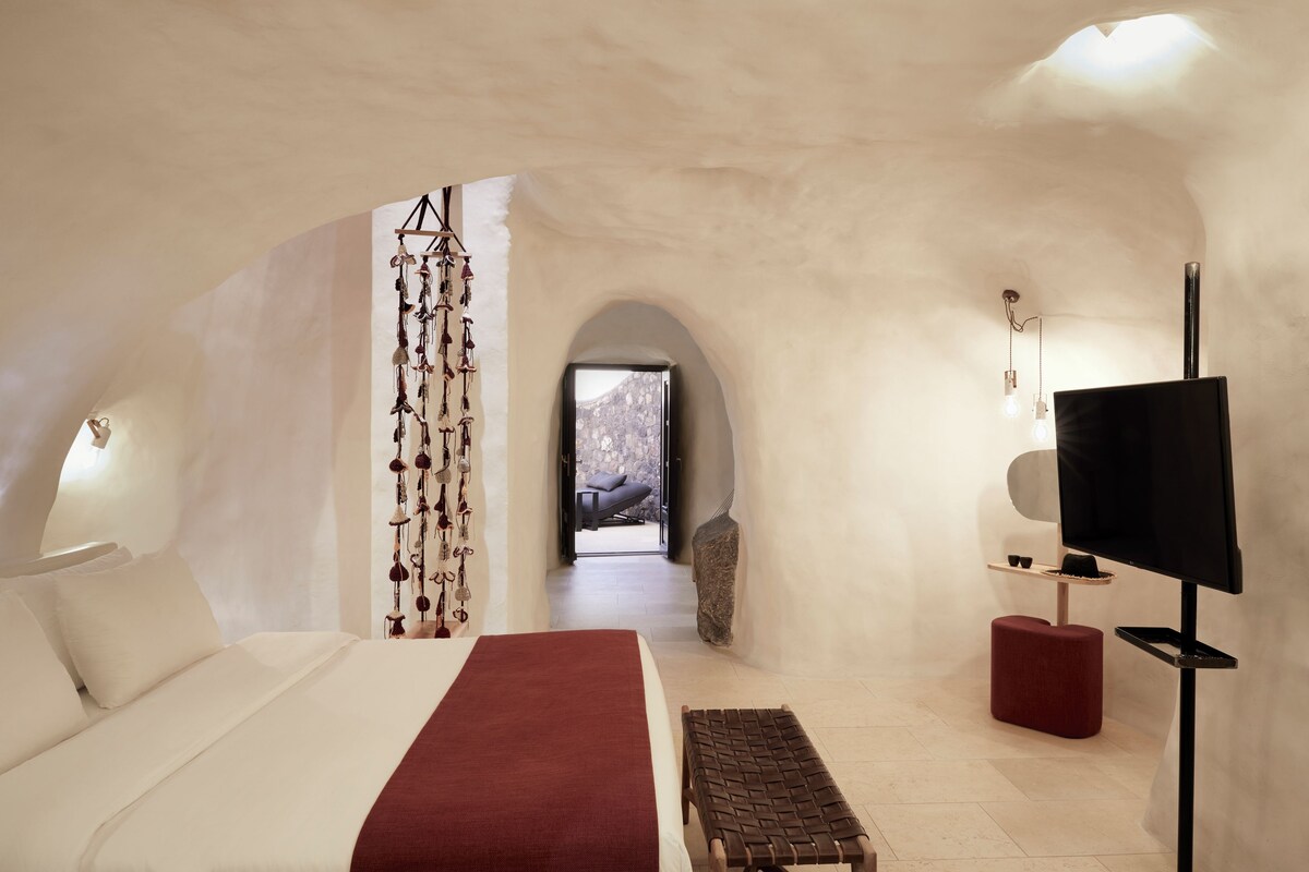A modern bedroom with a bed, a red bench, a TV, and a stone wall.