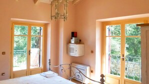 Quarto com teto de madeira, cama, radiador e janela com varanda.