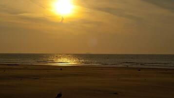 A beach with the sun setting over the horizon.