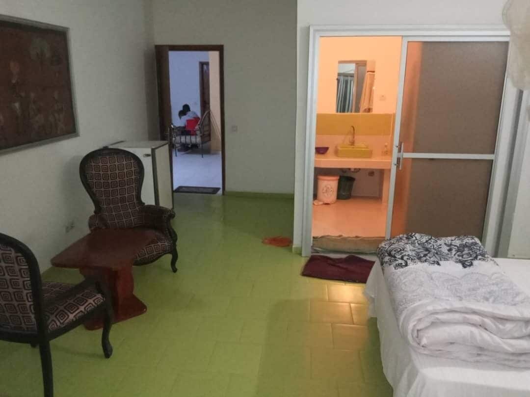 Une pièce comprenant un lit, deux fauteuils à motifs, une petite table et une armoire.
