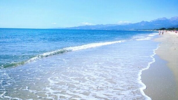Une plage à l’eau d’un bleu limpide, bordée d’un rivage sablonneux, avec des montagnes en toile de fond.
