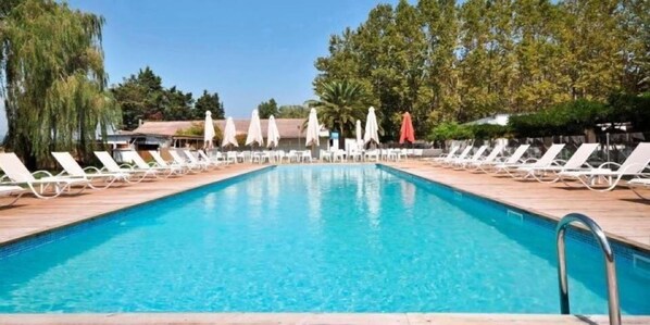 A rectangular swimming pool with white lounge chairs and umbrellas on either side.