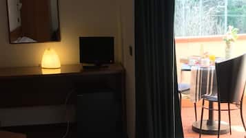 A hotel room with a bed, a desk with a lamp, a television, and a view of the outdoors through a window.