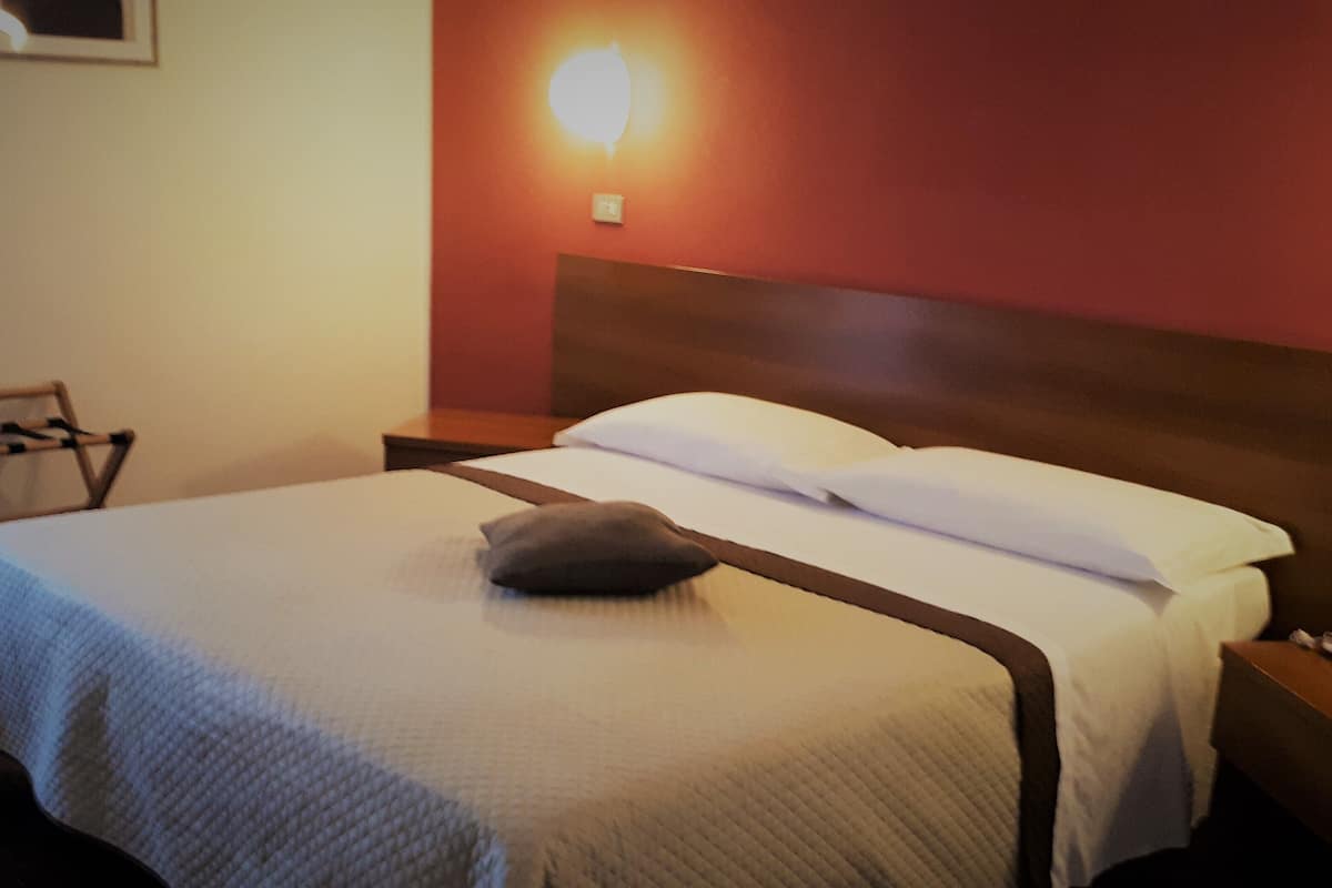 Un lit bien fait, avec un oreiller, une table de chevet sur laquelle se trouve un téléphone et une lampe fixée au mur.