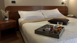 Ein ordentlich bezogenes Bett mit weißen Leinen, ein Tablett mit Croissants, einer Tasse und einem Glas Orangensaft darauf.