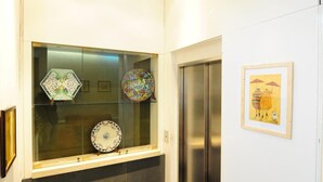 Ein Flur mit einer Glasvitrine, die dekorative Teller beherbergt, einem Wandbild und einem modernen Aufzug.