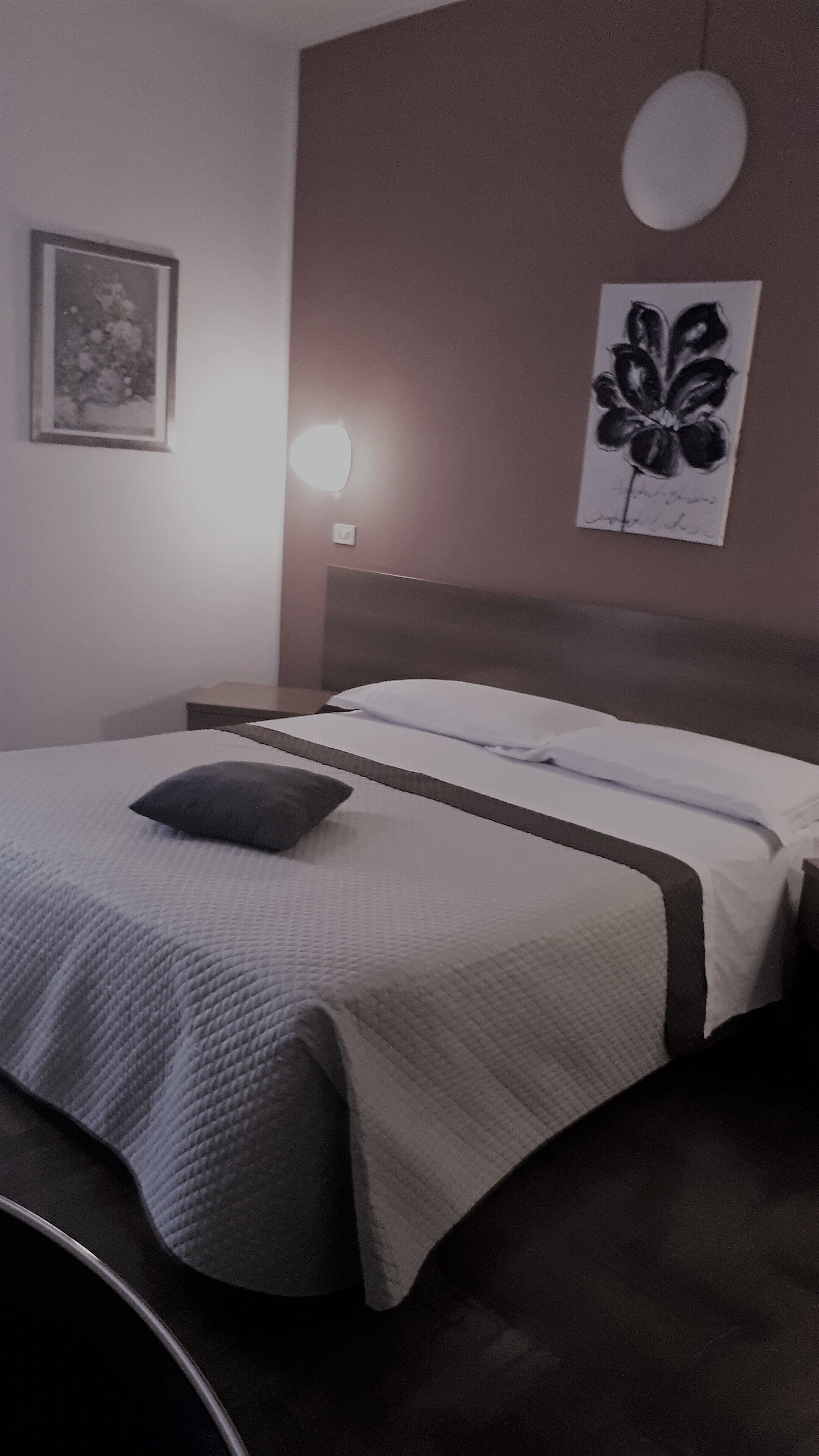 A neatly made bed with a pillow, a framed picture on the wall, and a wall-mounted light fixture.
