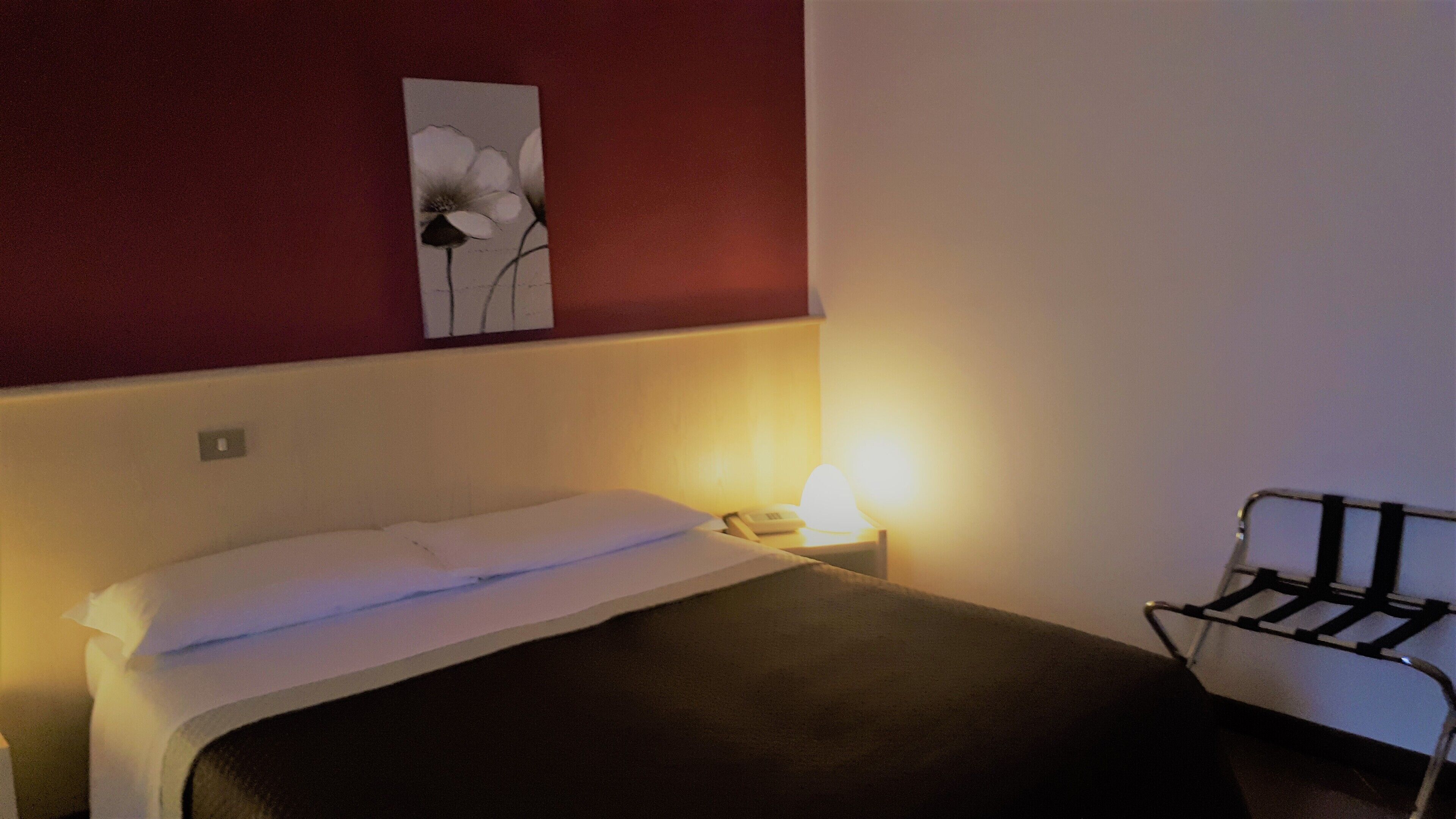 A hotel room with a bed, a bedside lamp, a chair, and a wall-mounted artwork.