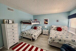 A bedroom with bunk beds, a dresser, a nightstand, a lamp, and a poster on the wall. - ENJOY FREE FUN DAILY & a tranquil Silver-rated condo with views of the ocean and lagoon. (Saint Augustine)