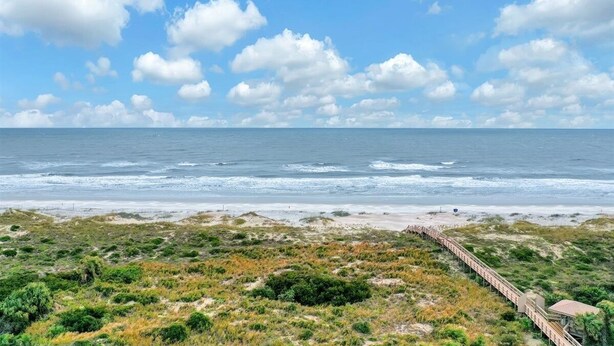 Eine Küstenlandschaft mit einem hölzernen Steg, der zu einem Strand führt, umgeben von viel Grün.