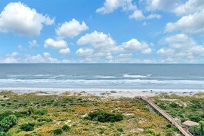 Een kustlandschap met een promenade die naar een strand leidt, onder een licht bewolkte lucht.