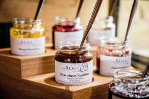 Una vitrina de madera con varios frascos de mermelada, cada uno etiquetado con el nombre 'Zur Rose' y distintos sabores como 'Mango-Konfitüre' y 'Johannisbeersirup'.