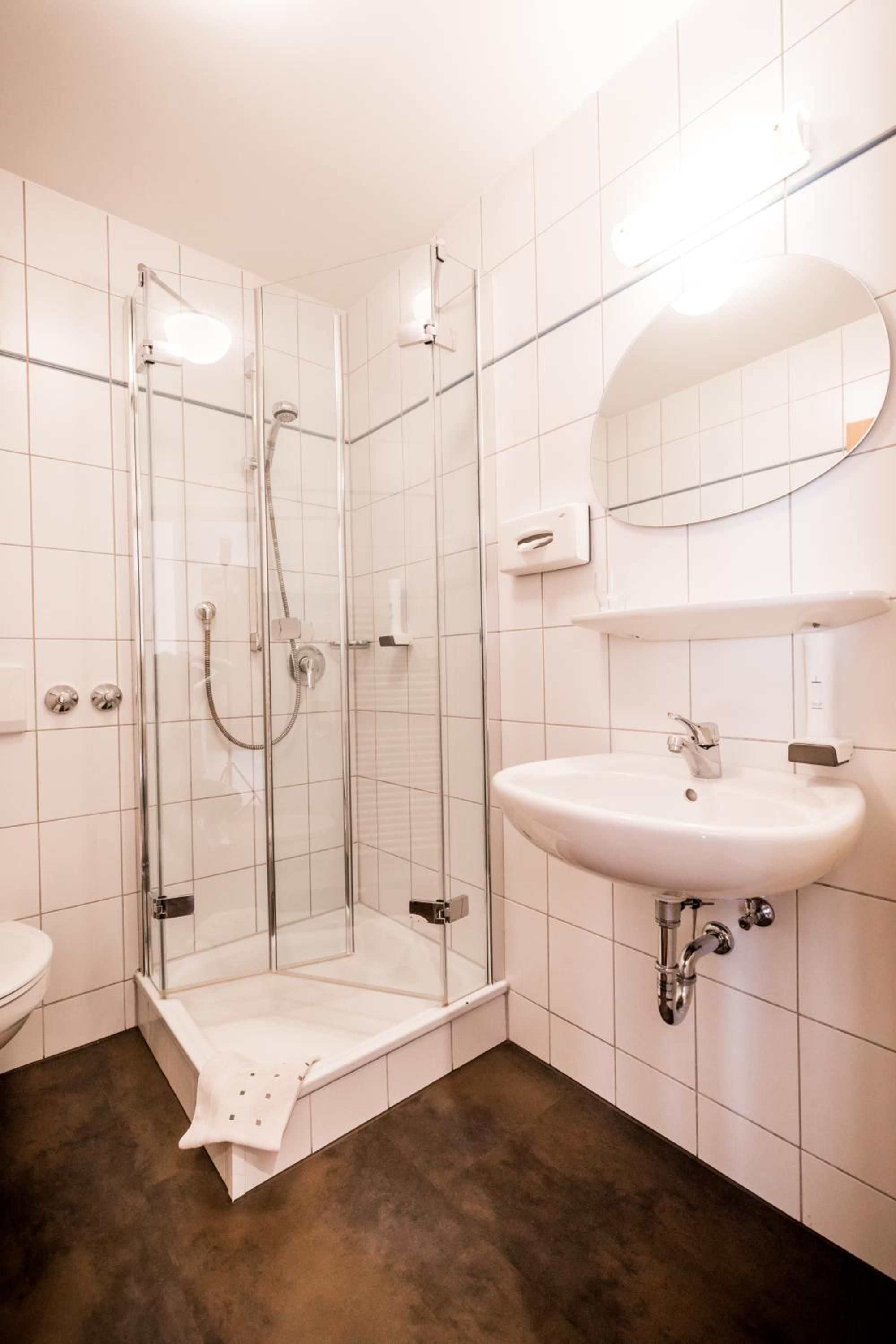 Ein modernes Badezimmer mit einer Duschkabine aus Glas, einem weißen Waschbecken und einem Spiegel darüber.