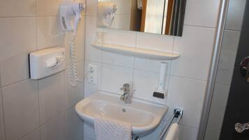 A bathroom with a white sink, a towel rack, a mirror, and a hairdryer mounted on the wall.