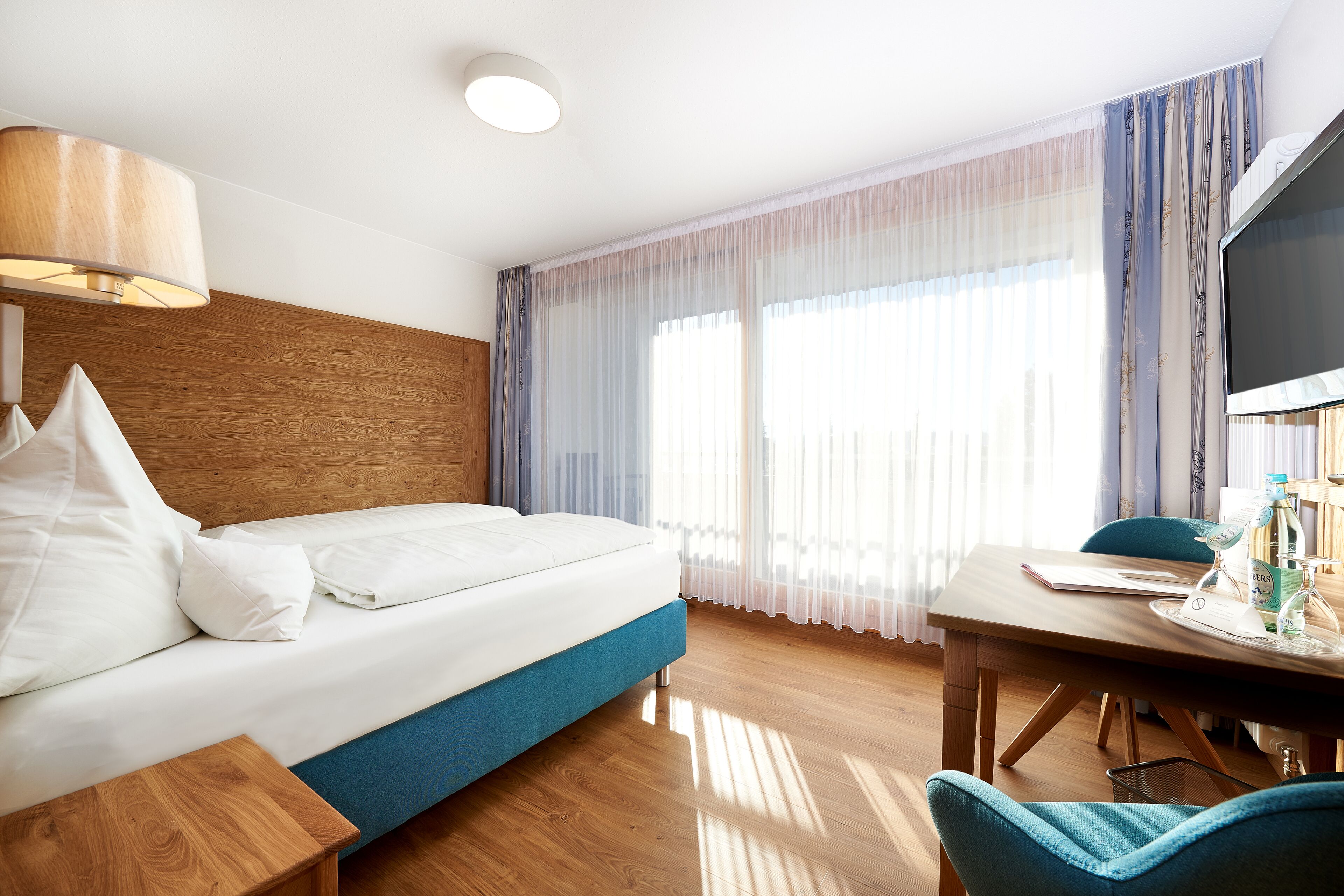 Una camera d'albergo con un letto, una testiera in legno, una scrivania con una sedia e un televisore.