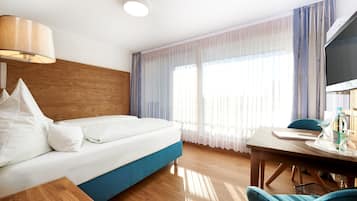 Una camera d'albergo con un letto, una testiera in legno, una scrivania con una sedia e un televisore.