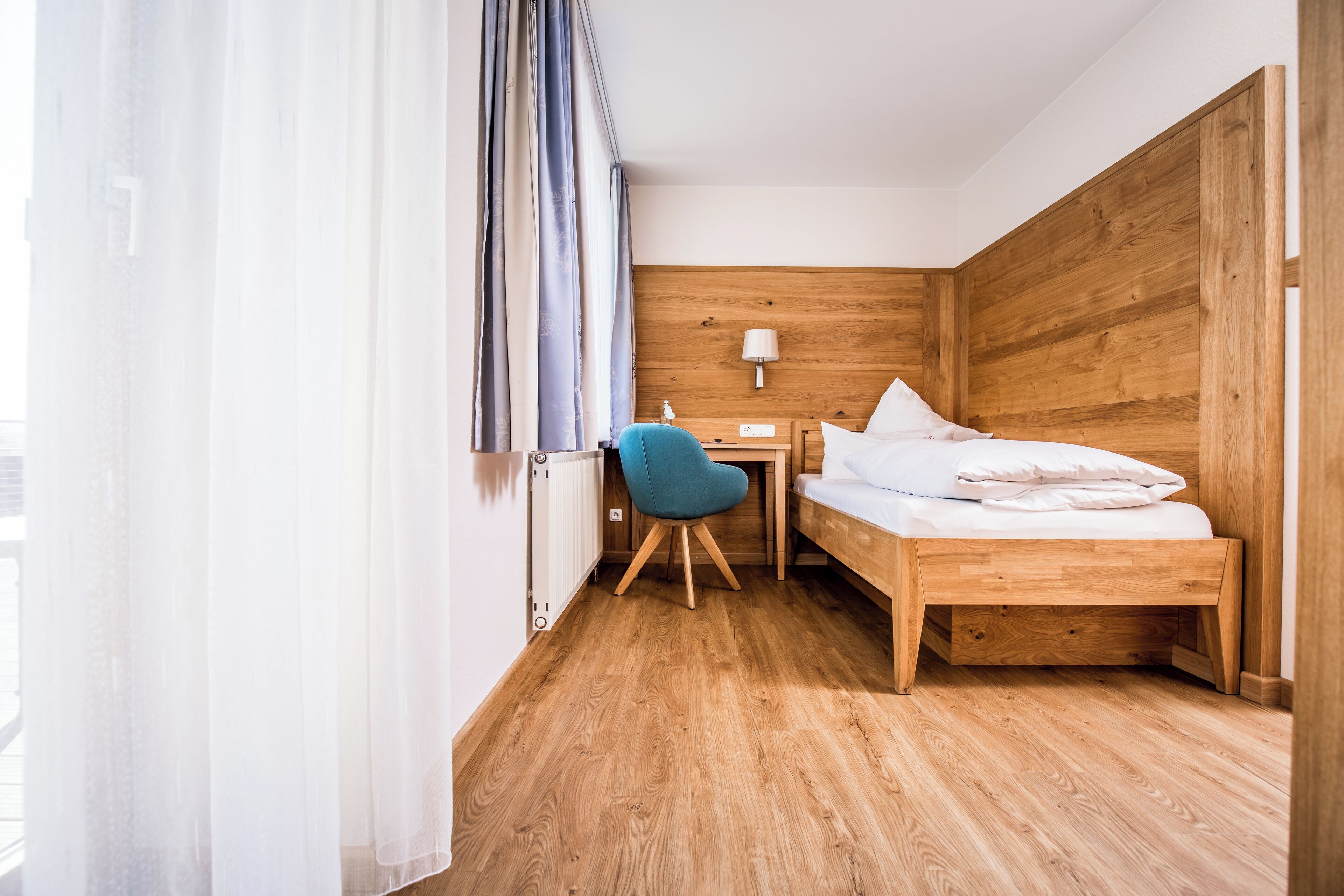 A small, modern hotel room with a wooden bed, a desk, and a chair.