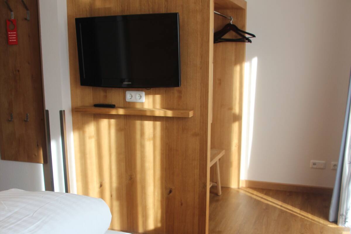 A modern room with a bed, a TV mounted on a wooden wall, a chair, and a wooden wardrobe.