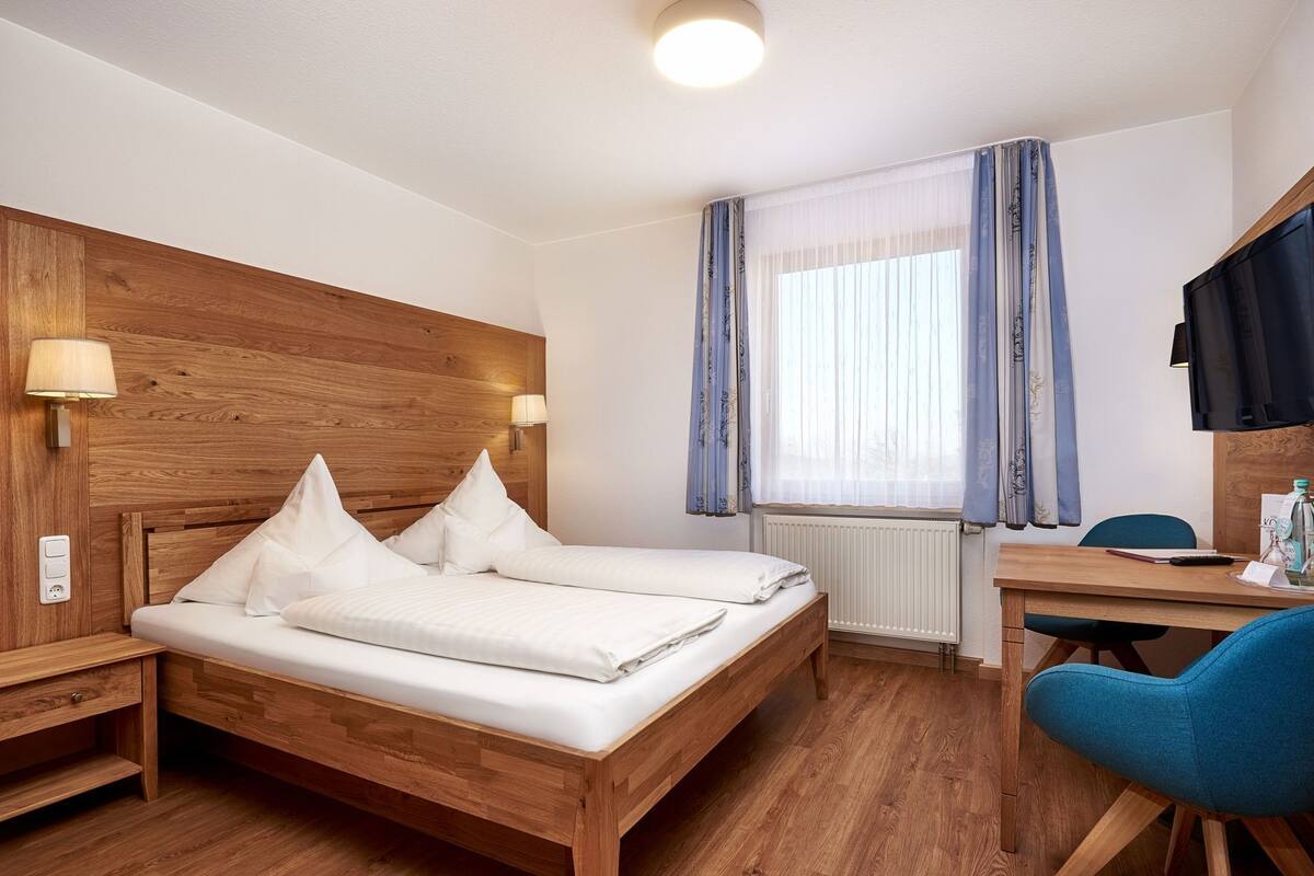 A hotel room with a wooden bed, a desk, a chair, and a window with curtains.
