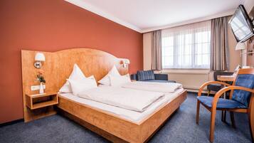 A hotel room with a wooden bed, a desk, a chair, a TV, and a window with curtains.