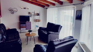 Una sala de estar moderna con techo de madera, sofás de cuero negro, una pequeña mesa de centro de madera, un televisor y una estantería.