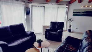 Una sala de estar moderna con un sofá de cuero negro, un sillón negro y una mesita redonda con una planta.