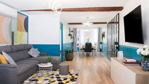 A modern living room with a sofa, coffee table, and a TV. There is a dining area in the background with a table and chairs. - Elegant, Air-conditioned & Central, close Marais (Paris)