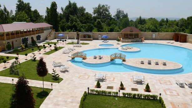 A large outdoor swimming pool with multiple sections and lounge areas, surrounded by well-maintained lawns and trees. - Qafqaz Yeddi Gozel Resort (Gabala)