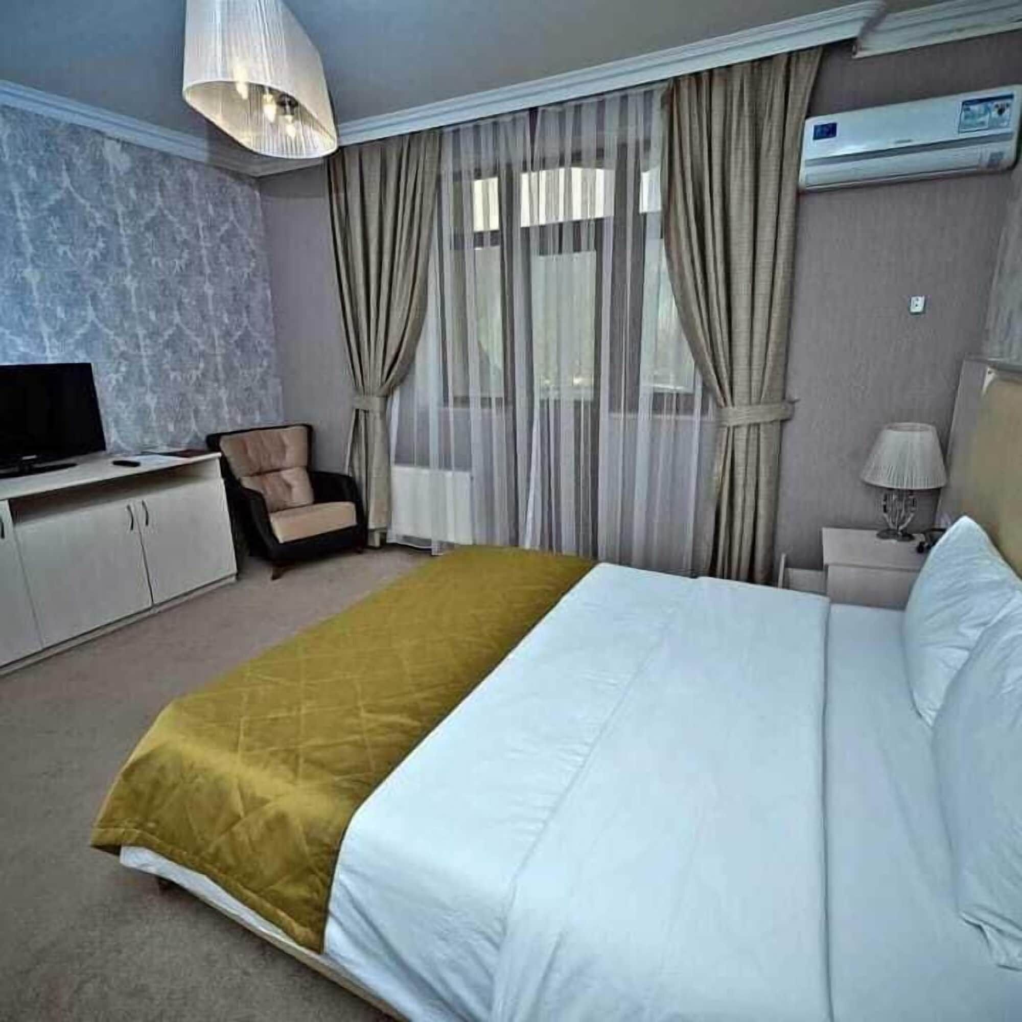 A hotel room with a bed, a TV, a chair, a lamp, and an air conditioning unit.
